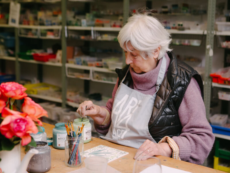 Elderly lady dipping a paint brush into a pot at a class